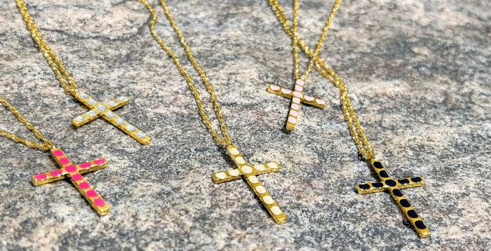 Four cross necklaces placed laying staggered on a rock.